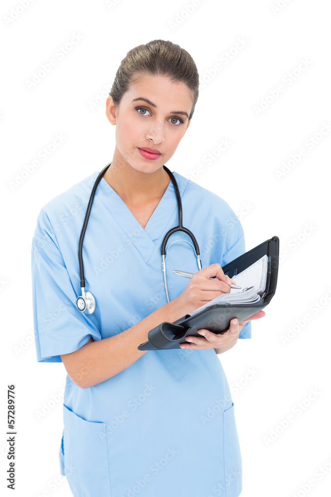 Stern brown haired nurse in blue scrubs filling an agenda Stern brown haired nurse in blue scrubs filling an agenda