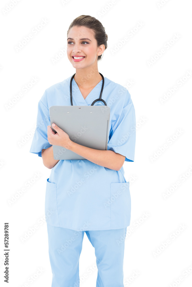 Thoughtful brown haired nurse in blue scrubs holding a clipboard Thoughtful brown haired nurse in blue scrubs holding a clipboard