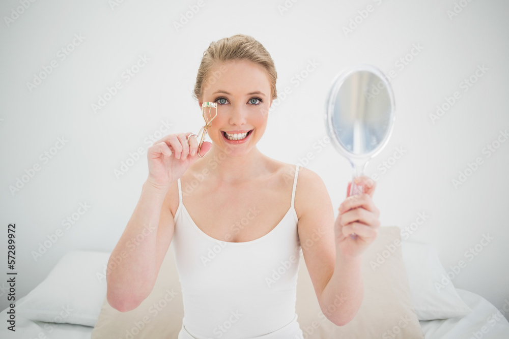 Natural happy blonde holding mirror and using eyelash curler Natural happy blonde holding mirror and using eyelash curler
