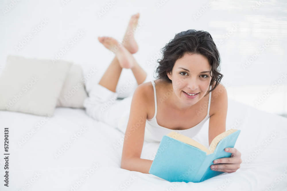 Content casual brunette in white pajamas relaxing on a bed readi Content casual brunette in white pajamas relaxing on a bed readi