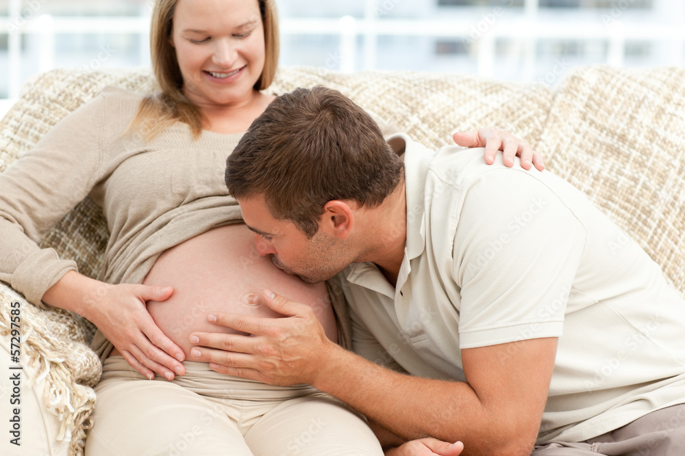 Future dad kissing the belly of his wife sitting on the sofa Future dad kissing the belly of his wife sitting on the sofa