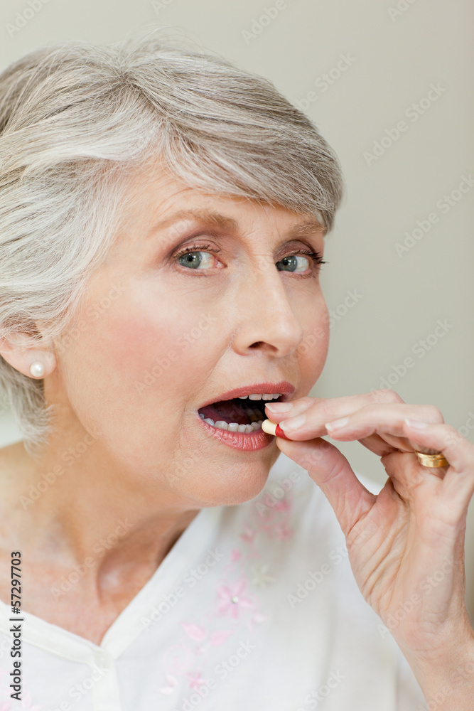 Senior woman looking at the camera while taking pill Senior woman looking at the camera while taking pill