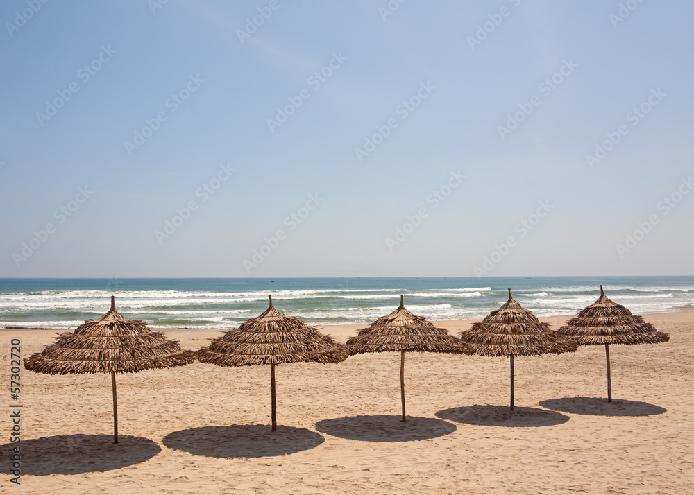 Blue sky as a background and row of straw umbrellas.