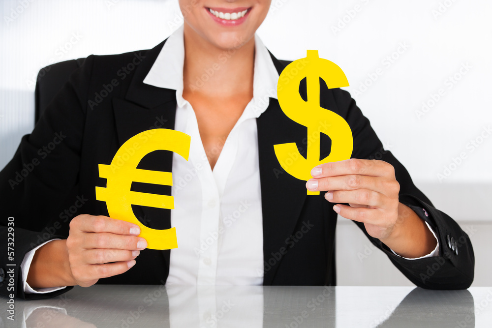 Businesswoman Holding Euro And Dollar Sign At Desk Businesswoman Holding Euro And Dollar Sign At Desk