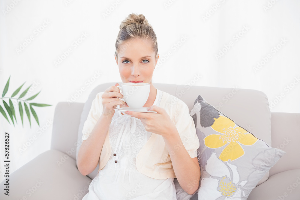 Charming fresh model drinking coffee sitting on sofa