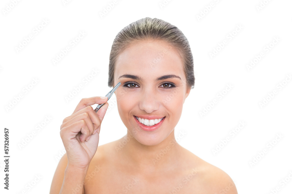 Smiling brunette woman plucking her eyebrows