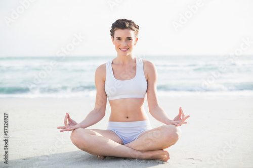 Smiling slim brown haired model in white sportswear meditating i © lightwavemedia