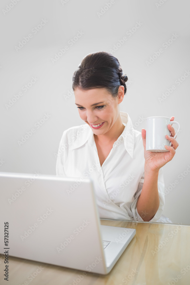 Smiling businesswoman working on laptop holding coffee Smiling businesswoman working on laptop holding coffee