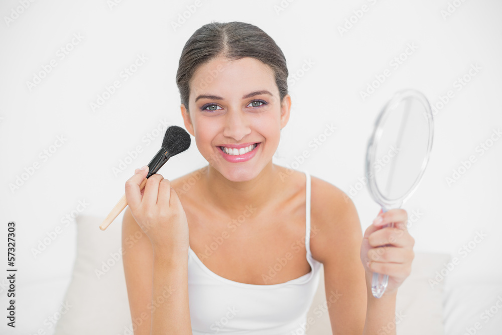 Happy young brown haired model in white pajamas applying powder Happy young brown haired model in white pajamas applying powder