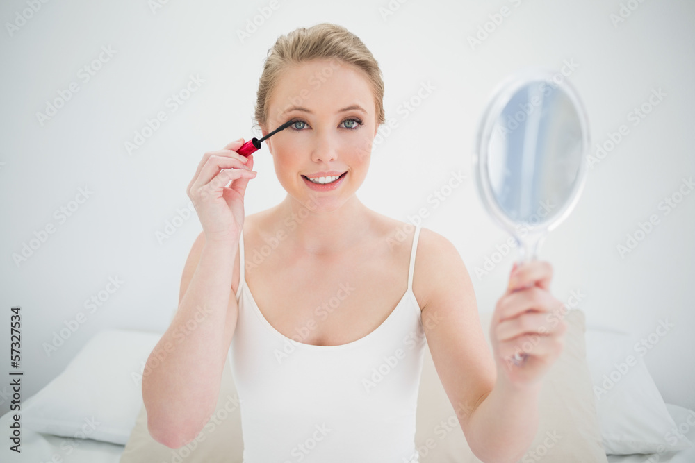 Natural smiling blonde holding mirror and applying mascara Natural smiling blonde holding mirror and applying mascara
