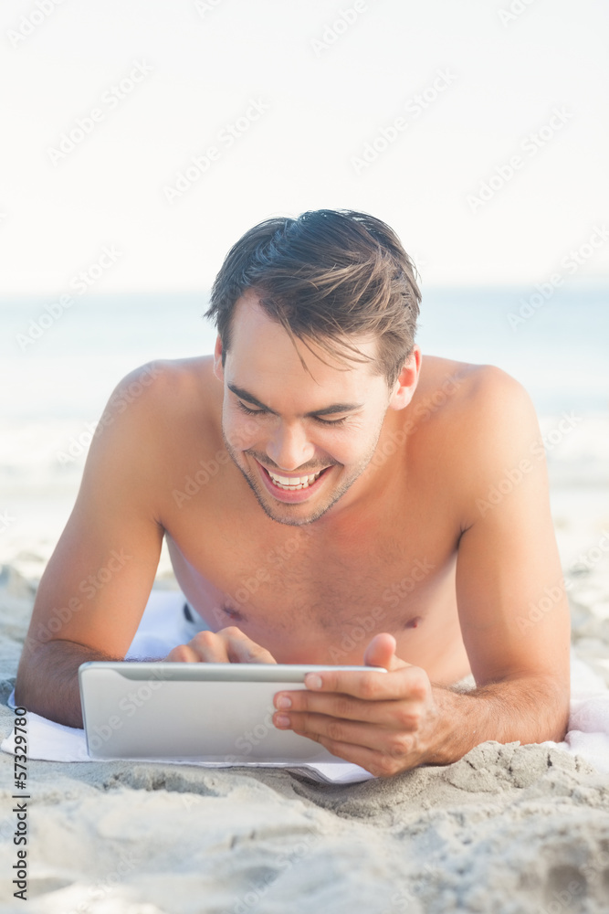 Handsome man lying on his towel using his tablet
