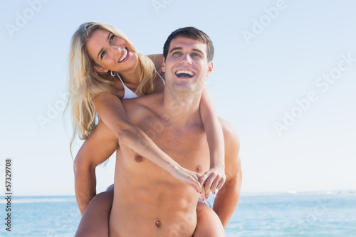 Laughing man giving his pretty girlfriend a piggy back smiling a