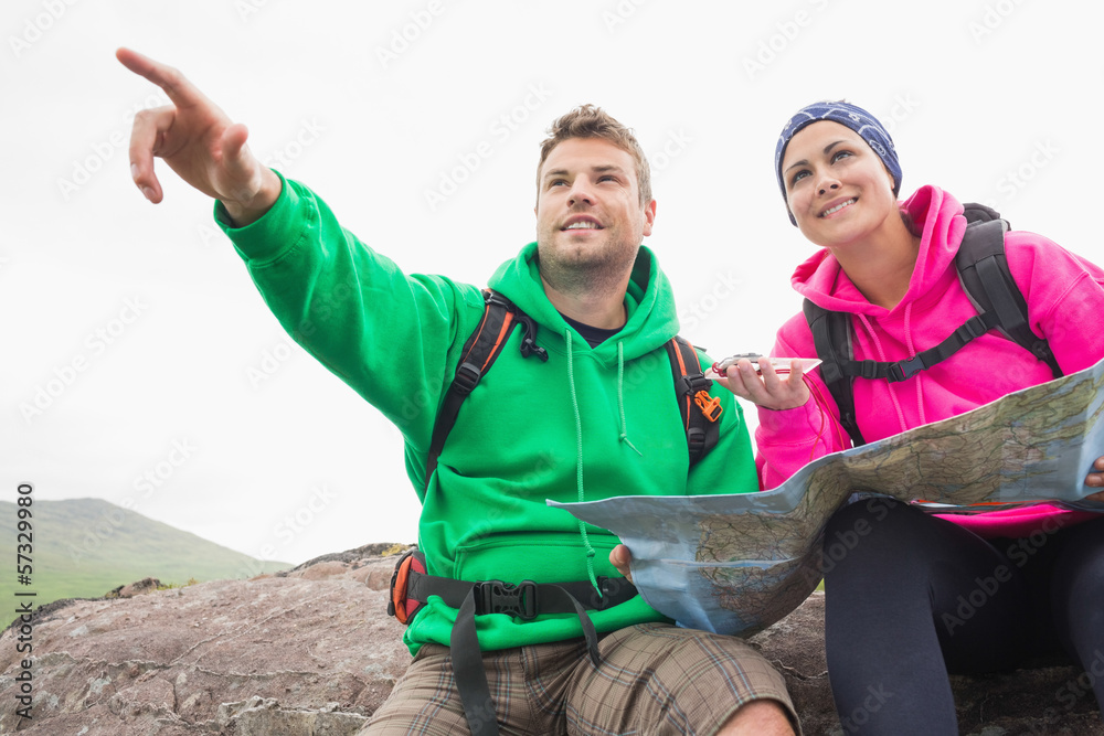 Couple using map and compass sitting on a rock with man pointing stock
