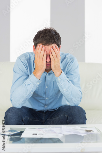 Troubled casual man sitting on couch paying bills