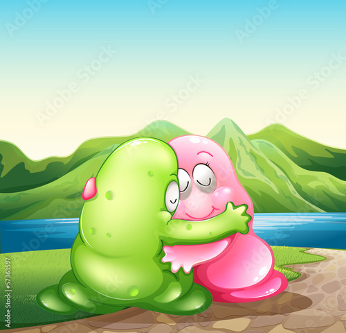 A green and a pink monster hugging each other at the riverbank