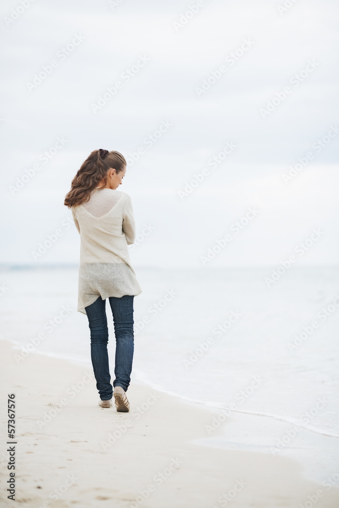 Thoughtful young woman in sweater walking on lonely beach