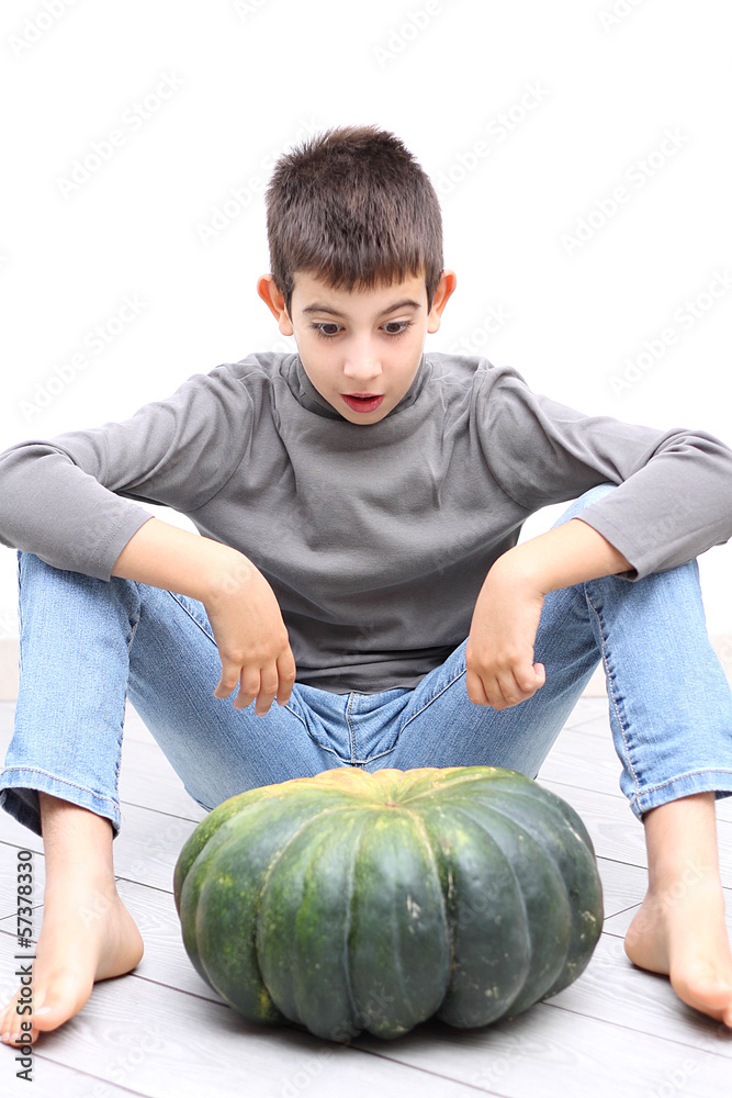 Fototapeta premium Young boy looking surprised at and big pumpkin