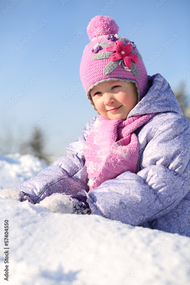 Smiling little girl dressed in pink scarf sits on snow Smiling little girl dressed in pink scarf sits on snow