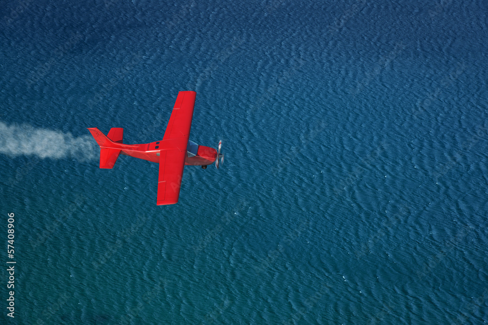 Fototapeta premium small red airplane flies over a sea