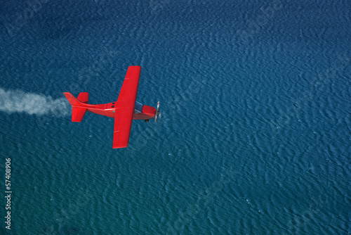 small red airplane flies over a sea