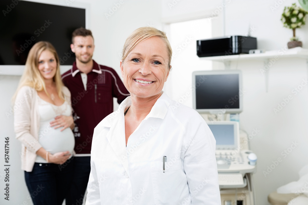 Fototapeta premium Happy Doctor With Expectant Couple In Background