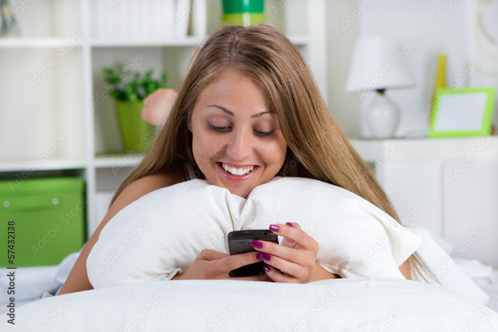 young smiling woman looking at her phone on the bed young smiling woman looking at her phone on the bed