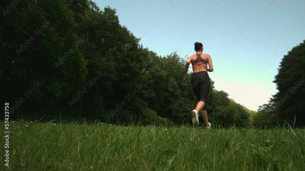 Low angle view of sporty womans back running on grass Low angle view of sporty womans back running on grass