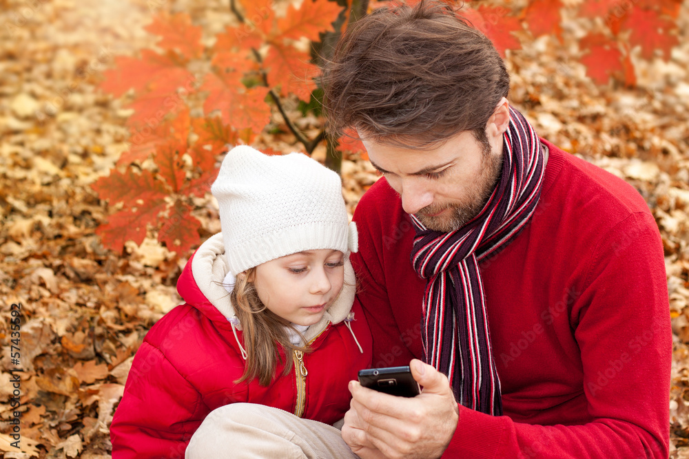 Father and daughter looking at phone in an autumn park