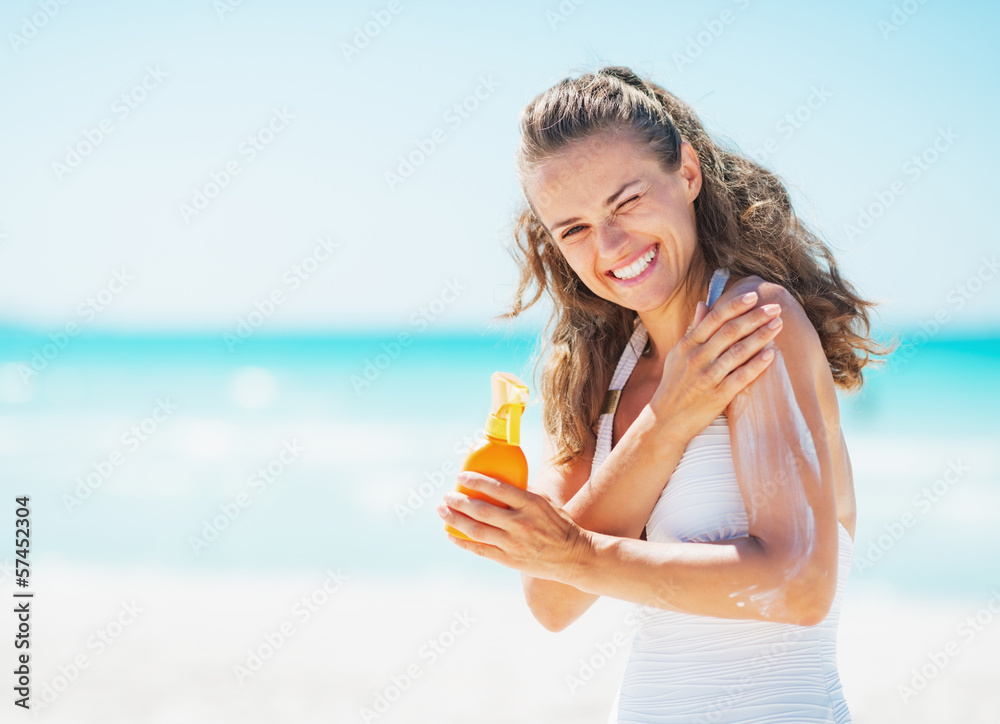 Smiling young woman applying sun block creme on beach Smiling young woman applying sun block creme on beach