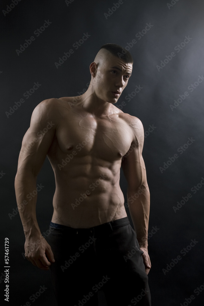 Young sexy man with athletic body on black background