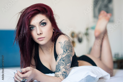 Intimate portrait of beautiful girl with tattoo lying on bed.