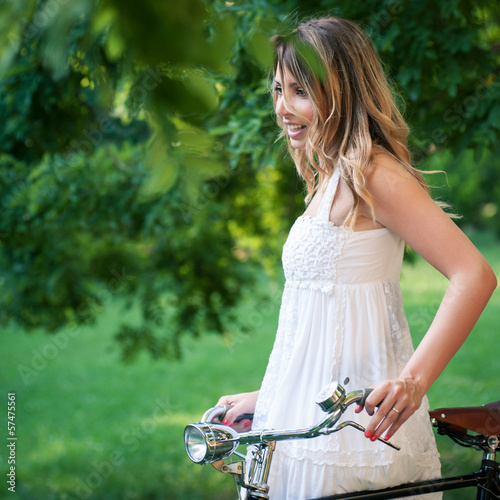 Beautiful young woman portrait with bicycle in a park.