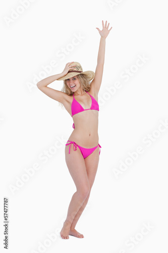 Smiling young woman holding her hat with one arm raised