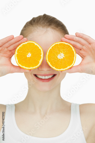 Close up of a woman placing oranges on her eyes