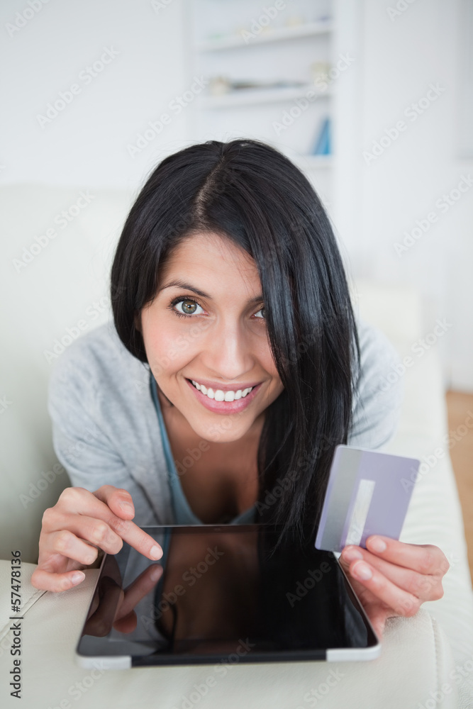 Woman smiling while holding a credit card and touching a tablet Woman smiling while holding a credit card and touching a tablet