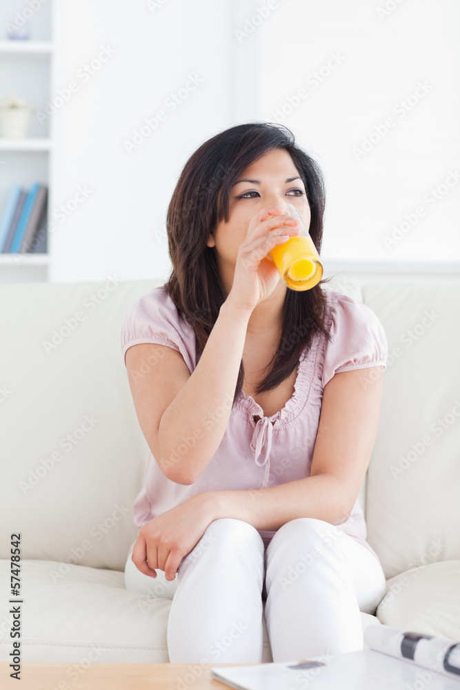 Woman sitting on a couch while drinking a glass of orange juice Woman sitting on a couch while drinking a glass of orange juice