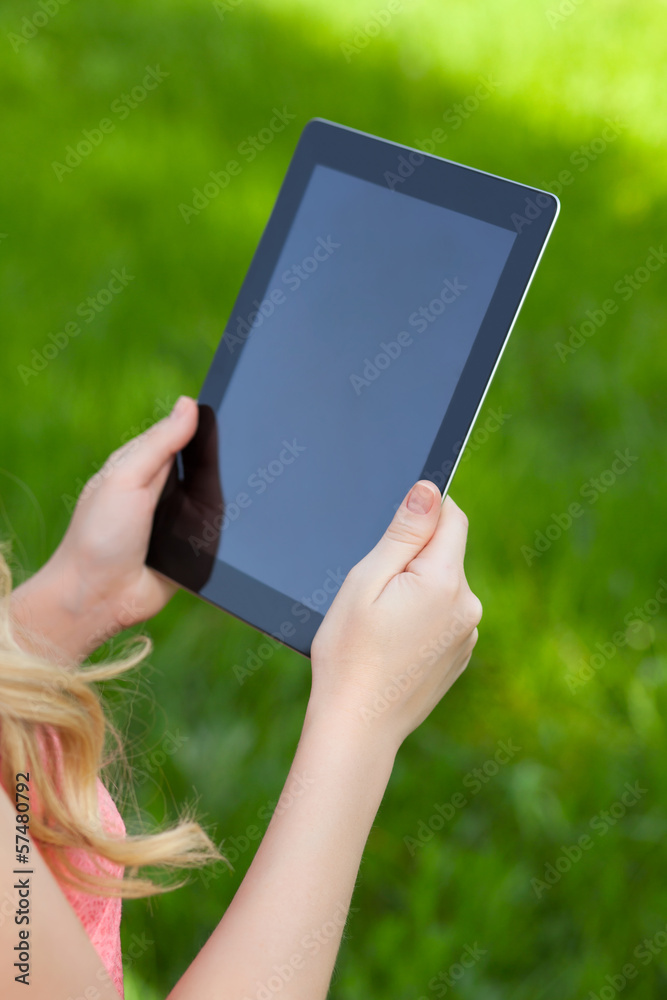 girl holds a tablet on a background of green grass