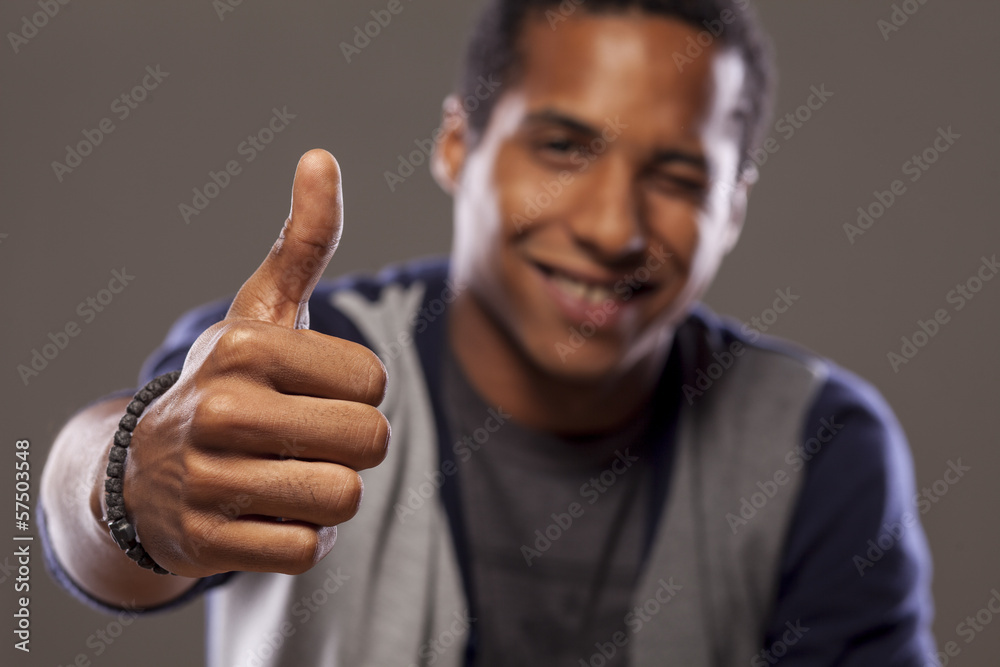 smiling dark-skinned young man showing thumbs up and winks smiling dark-skinned young man showing thumbs up and winks