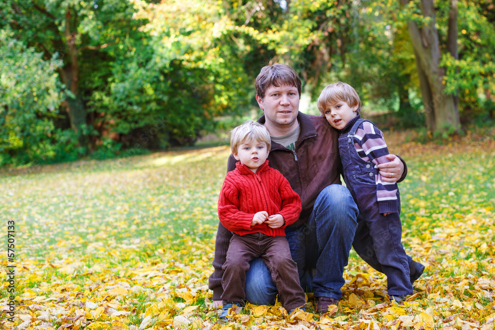 Fototapeta premium Happy father with two little sons having fun in autumn park.
