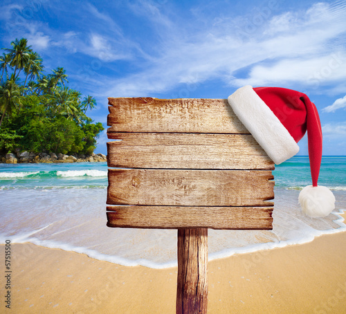 Christmas on beach. Wooden signboard with Santa's hat.