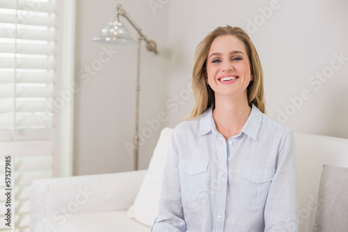 Casual laughing blonde sitting on couch looking at camera