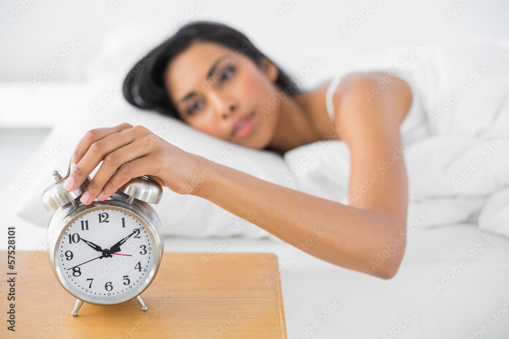 Attractive tired woman turning off the alarm clock Attractive tired woman turning off the alarm clock
