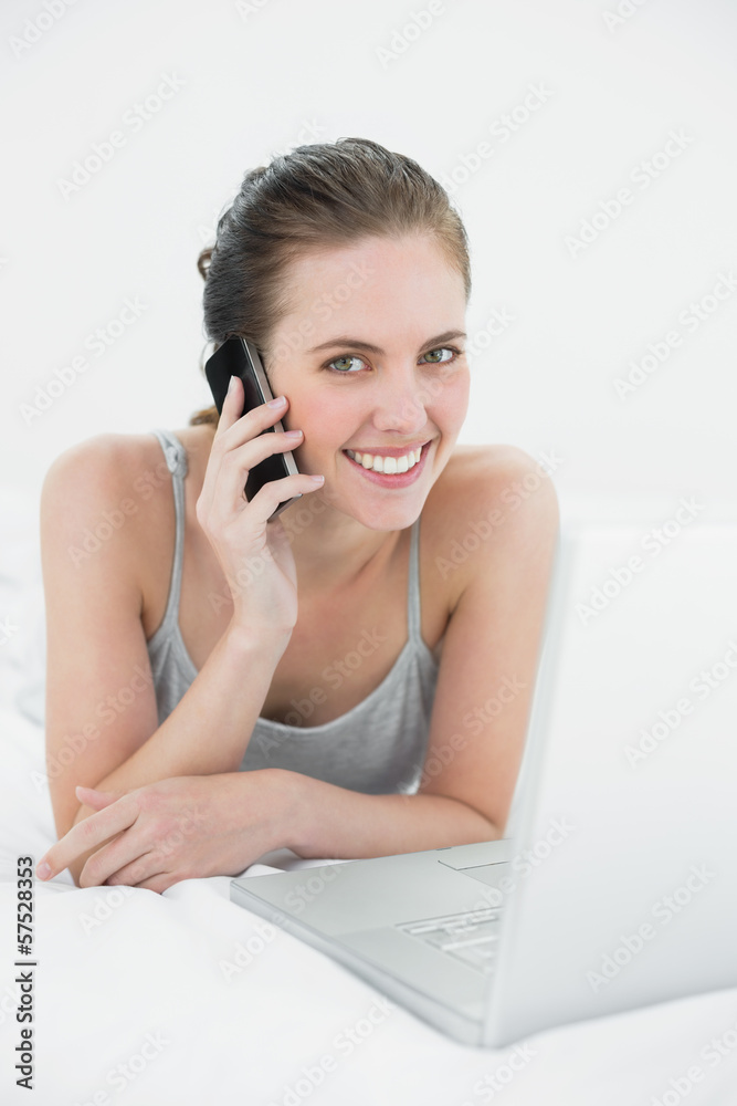 Smiling casual woman using cellphone and laptop in bed Smiling casual woman using cellphone and laptop in bed