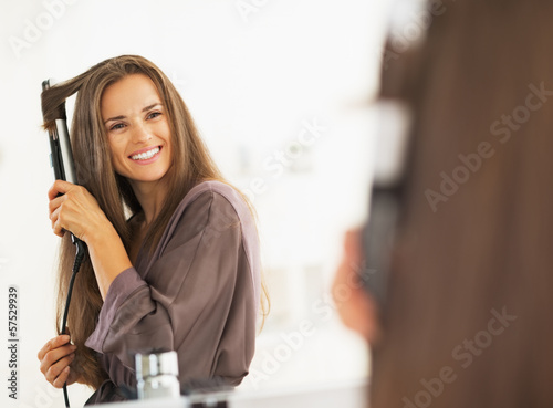 Smiling woman curling hair with straightener