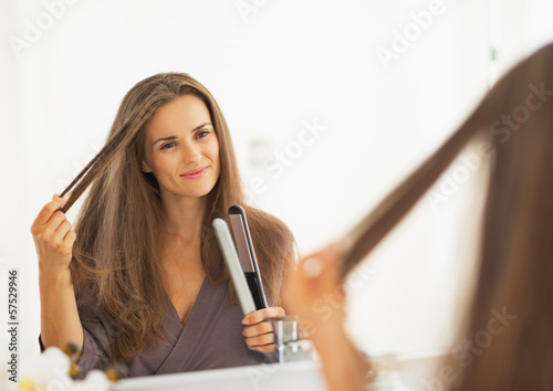 Happy young woman checking hair after straightening