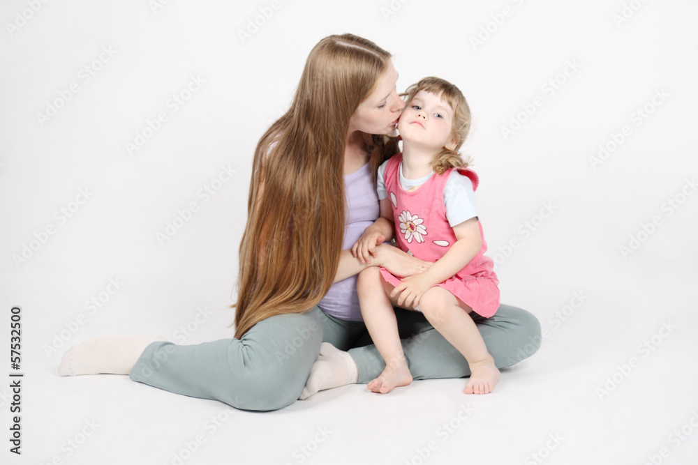 Pregnant woman sits on floor and kisses her little daughter on g