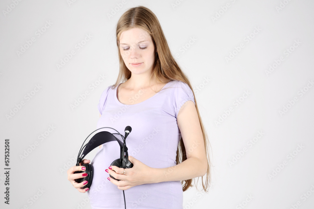 Pregnant beautiful woman put big black headphones to belly on gr Pregnant beautiful woman put big black headphones to belly on gr