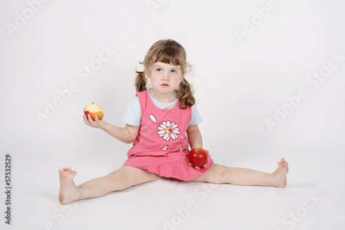 Little beautiful girl eats apple and holds second apple on floor