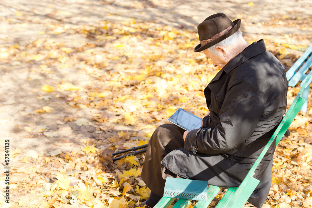 Elderly one legged man sitting reading in the park