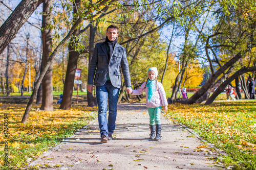Adorable little girl with happy father walking in autumn park on